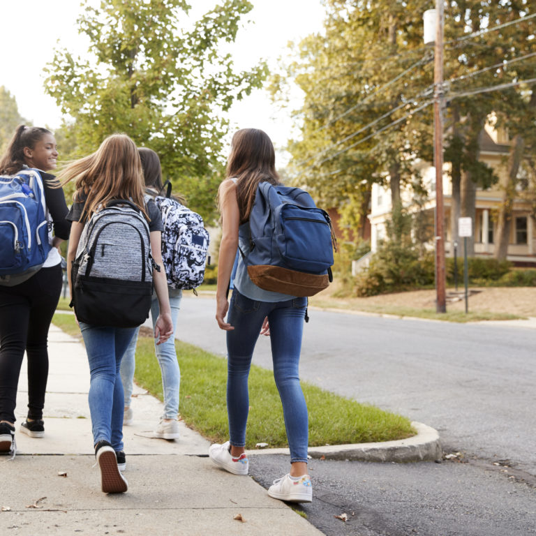 Four young teen girls walking to school together, back view