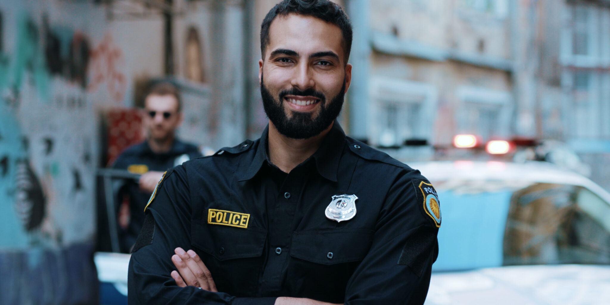 Smiling young man cops stand near patrol car look at camera enforcement happy officer police uniform auto safety security communication control policeman portrait close up slow motion police officer