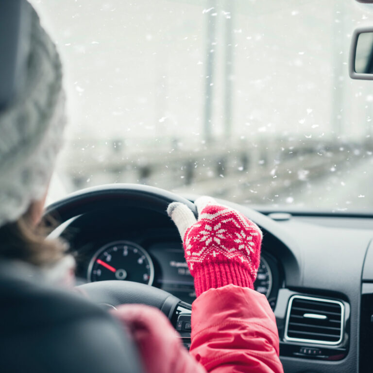 Woman in the red jacket, hat and christmas gloves is driving on the highway at the winter snowfall.  View from the back seat of the car. concept.